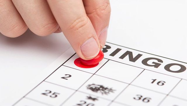 Placing red bingo marker on printed card close-up finger pressing game token for winning