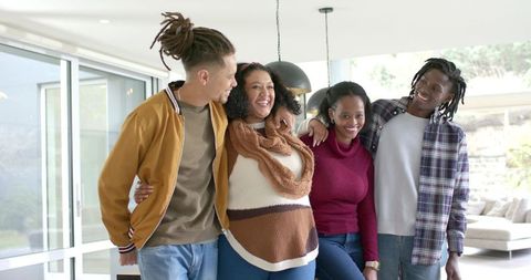 Laughing diverse friends linking arms in modern living room showing togetherness