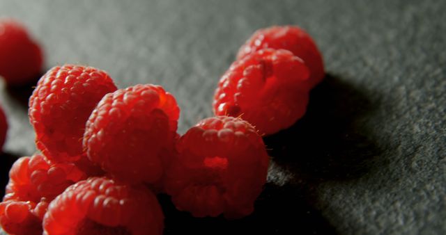 Close-up of ripe raspberries on a dark surface, with copy space. Their rich red color and delicate texture are highlighted by the contrasting background.