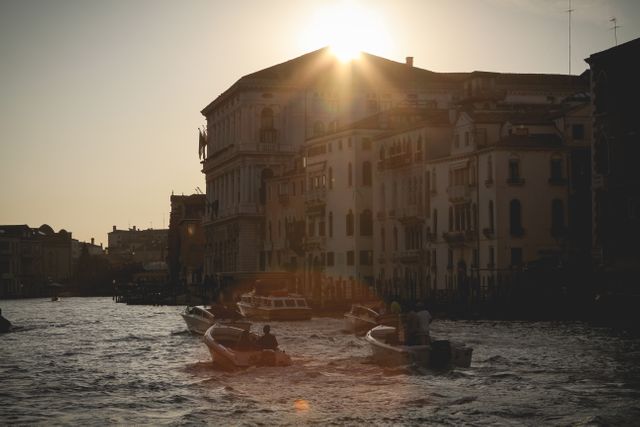 Boats moving on Venetian canal with historical buildings in background during sunrise, showcasing calm waterway and early morning light. Ideal for travel blogs, Italy tourism promotions, and European architecture publications.