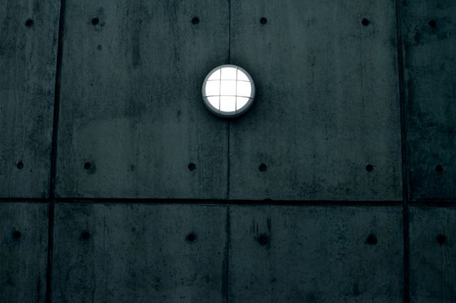 Minimalist concrete wall featuring an illuminated round light fixture. The industrial design and geometric pattern lend a modern and symmetrical ambiance. Ideal for backgrounds, design inspiration, architectural studies, and minimalistic themed projects.