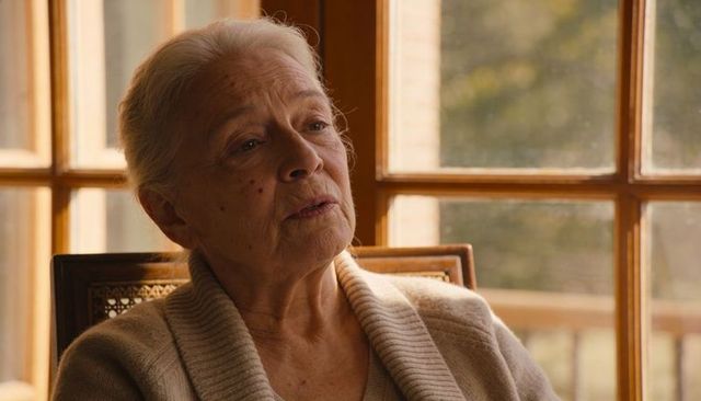Senior woman gazing thoughtfully by sunlit window in cozy beige cardigan, contemplative