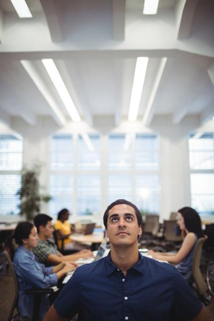 Man looking up while colleagues working in background at the office