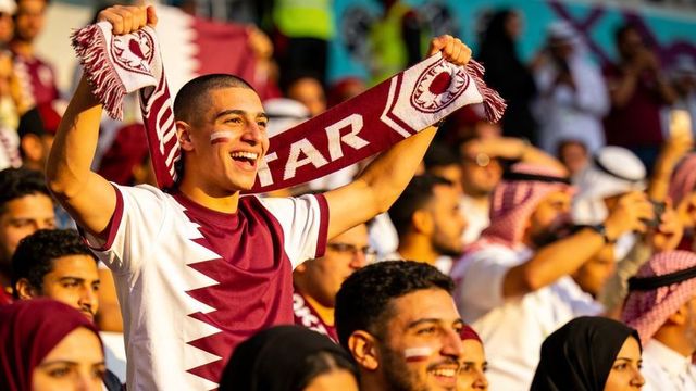 Cheering qatari football fans holding qatar scarf and wearing maroon jerseys