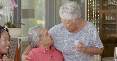 Senior couple sharing warm embrace while leaning and holding wine during family gathering