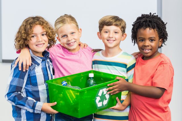Diverse group of children smiling and holding a green recycling bin filled with plastic bottles. Ideal for educational materials, environmental campaigns, and promoting sustainability and teamwork among young students.