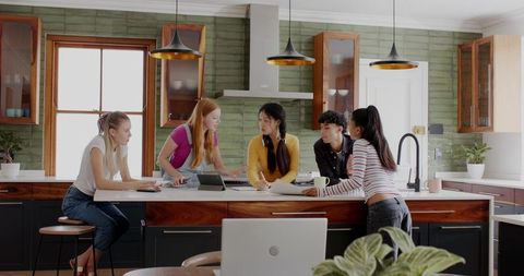 Diverse peers collaborating at modern kitchen island, sharing tablet, laptop and notes