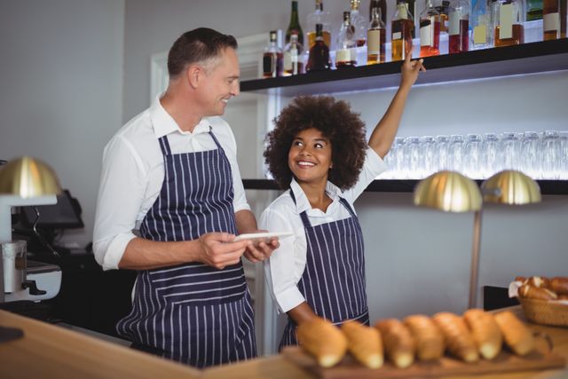 Waiter and waitress in uniform interacting at restaurant counter. Ideal for illustrating teamwork, customer service, and hospitality in a restaurant setting. Suitable for use in articles, advertisements, and promotional materials related to the food and beverage industry.