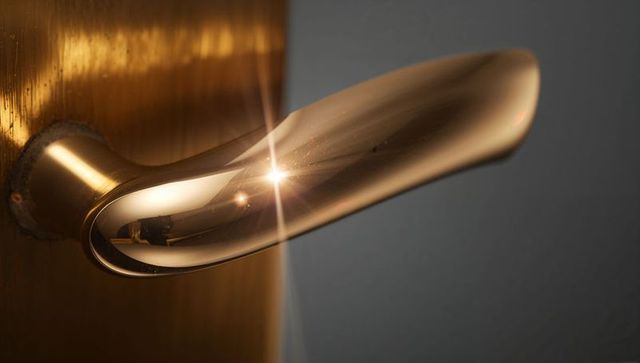 Polished brass door lever catching starburst glint on wood door edge closeup luxury