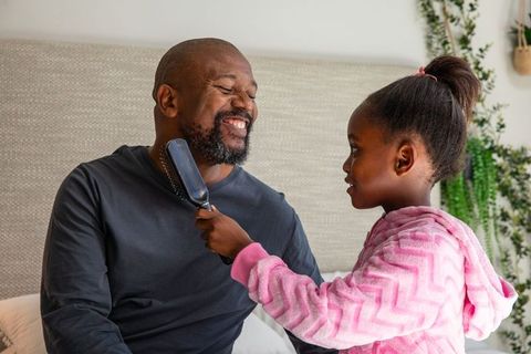 African american father and daughter brushing beard, sharing laughter in cozy bedroom