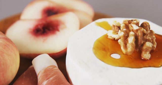 A close-up view showcases a plate with cheese, walnuts, and honey, accompanied by slices of peach, highlighting a gourmet snack or appetizer setup. The composition emphasizes the textures and colors of the fresh ingredients, inviting a sensory experience.