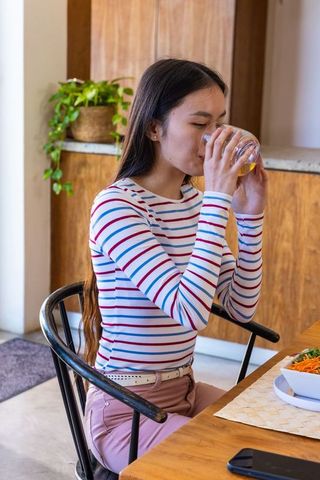 Young Woman Enjoying Refreshing Drink with Smartphones and Salad on Wooden Table