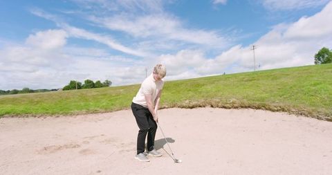 Male golfer preparing swing in sand bunker on bright day