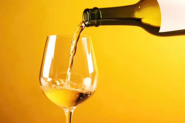 White wine pouring into clear glass against vibrant yellow background, perfect for illustrating concepts of celebration, alcohol consumption, stylish gatherings, wine tasting events, and summer refreshment imagery.