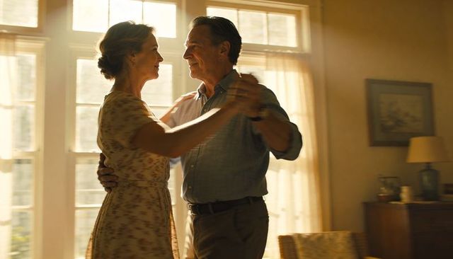 Sunlit senior couple dancing slowly in cozy living room tender embrace under golden light