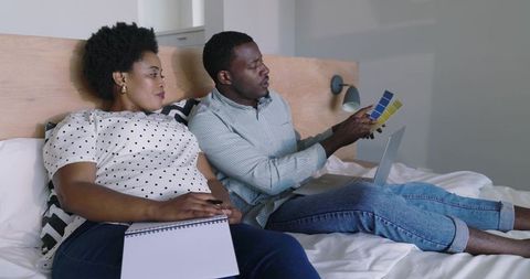 African american couple choosing paint swatches for bedroom renovation with laptop