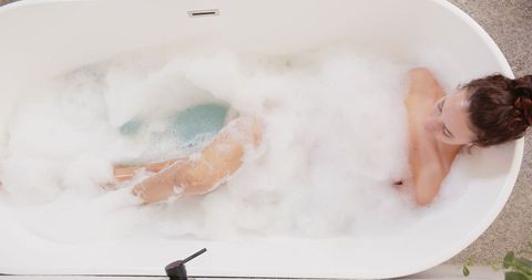 Woman Relaxing in Bubble Bath in Minimalist Bathroom