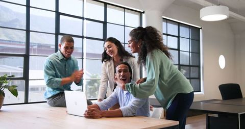 Diverse Team Celebrating Success at Work Around Laptop