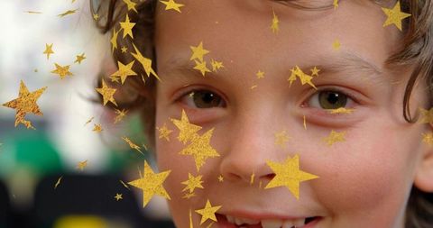Curly light-brown haired boy smiling at outdoor party with gold star stickers closeup