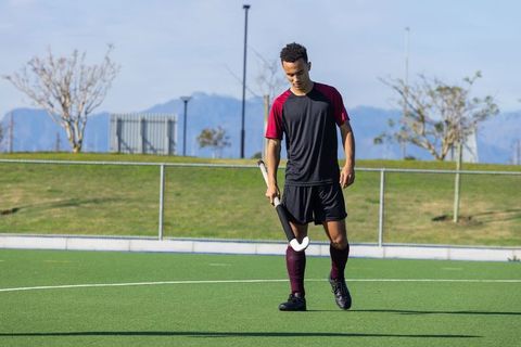 Athletic man working out on turf field with hockey stick outdoors
