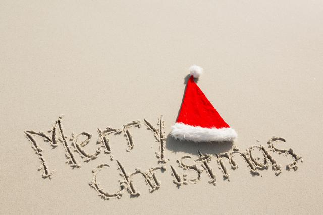 Merry Christmas written in sand with a Santa hat on a beach. Perfect for holiday greeting cards, travel advertisements, and festive social media posts. Ideal for conveying a warm, tropical holiday spirit.