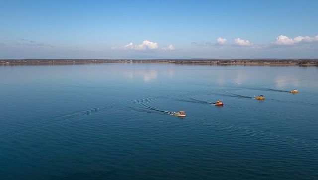 Small motorboats cutting across calm lake creating v-shaped wakes under clear blue sky