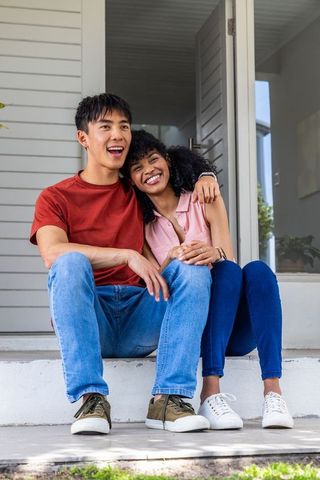 Young multiracial couple sitting on front steps sharing laughter and affectionate embrace