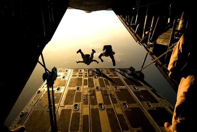 Paratroopers are jumping from a cargo aircraft during an early morning mission, silhouetted by a beautiful sunrise in the background. This could be used for themes related to military training, adventure sports, teamwork, and aviation safety. It's ideal for illustrating the bravery and skill required in paratrooper operations, defense tactics, and patriotic endeavors.