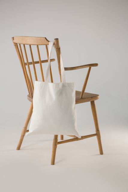 White bag hanging on a wooden chair against white background