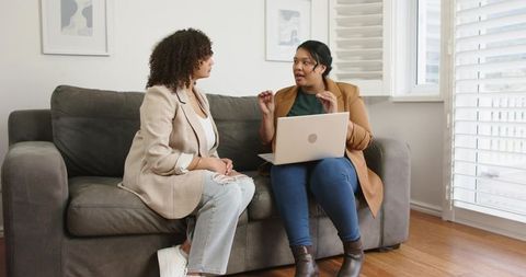 Women Collaborating on Laptop on Sofa Home Consultation and Professional Discussion