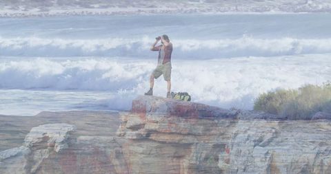 Explorer scanning ocean waves on rockies with binoculars