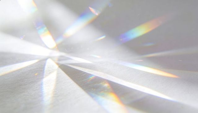 Prism casting refracted light rays forming soft rainbow spectrum on pale tabletop