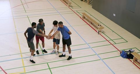 Teammates huddling over basketball on indoor court showing unity and motivation