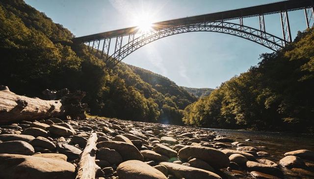 Sunburst Over Steel Arch Bridge Casting Golden Light Across Rocky Riverbed