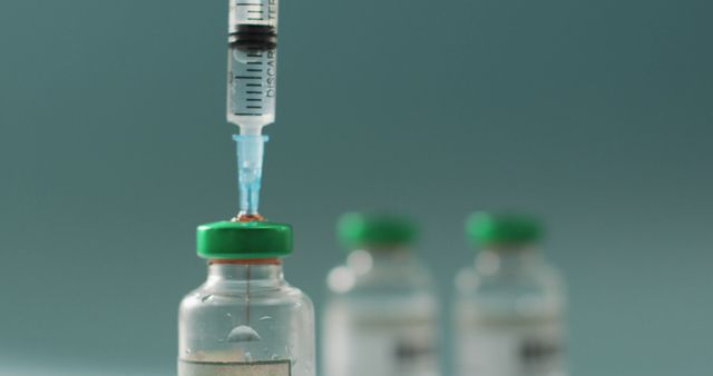 Close-up of a syringe drawing liquid from a vaccine vial with two vials blurred in the background. Suitable for topics on vaccination, medical procedures, healthcare, immunization, and medication. Ideal for use in articles, presentations, and educational materials related to vaccines and medical treatments.