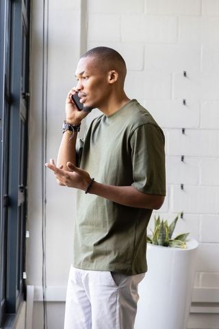African american man talking on phone by window in loft workspace gesturing casually