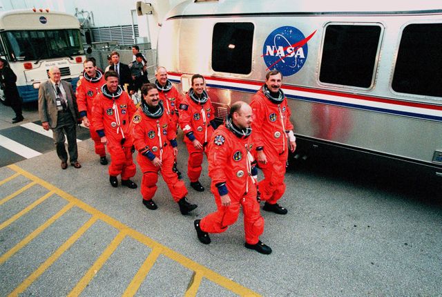 The STS-103 crew head for the Astrovan that will take them to Launch Pad 39B and more Terminal Countdown Demonstration Test (TCDT) activities. From left to right are (front row) Mission Specialists Steven L. Smith, C. Michael Foale (Ph.D.), and John M. Grunsfeld (Ph.D.), and Pilot Scott J. Kelly; (back row) Mission Specialists Claude Nicollier of Switzerland and Jean-François Clervoy of France, who are with the European Space Agency, and Commander Curtis L. Brown Jr. The TCDT provides the crew with emergency egress training, opportunities to inspect their mission payloads in the orbiter's payload bay, and simulated countdown exercises. STS-103 is a "call-up" mission due to the need to replace and repair portions of the Hubble Space Telescope, including the gyroscopes that allow the telescope to point at stars, galaxies and planets. The STS-103 crew will be replacing a Fine Guidance Sensor, an older computer with a new enhanced model, an older data tape recorder with a solid-state digital recorder, a failed spare transmitter with a new one, and degraded insulation on the telescope with new thermal insulation. The crew will also install a Battery Voltage/Temperature Improvement Kit to protect the spacecraft batteries from overcharging and overheating when the telescope goes into a safe mode. Four EVA's are planned to make the necessary repairs and replacements on the telescope. The mission is targeted for launch Dec. 6 at 2:37 a.m. EST