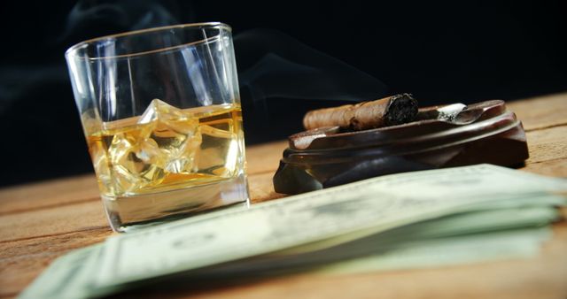 Close-up of ashtray, cigar, whisky and US dollars on table