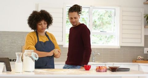 Diverse couple baking together in bright home kitchen, woman kneading dough at island