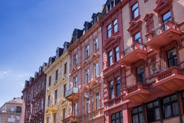 Colorful historic buildings stand in line under a clear blue sky in a European city. Each building has a distinct color, contributing to a vibrant cityscape. Perfect for use in travel guides, architectural showcases, and urban living blogs to depict the charm and vibrancy of European city life.