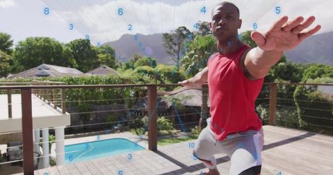Balancing athletic man practicing yoga on wooden deck overlooking pool and tropical garden