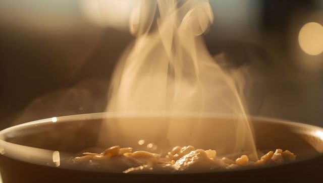 Steaming oat porridge in ceramic bowl backlit morning breakfast closeup warm cozy bokeh