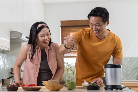 Asian couple preparing healthy green smoothie together in bright modern kitchen with blender