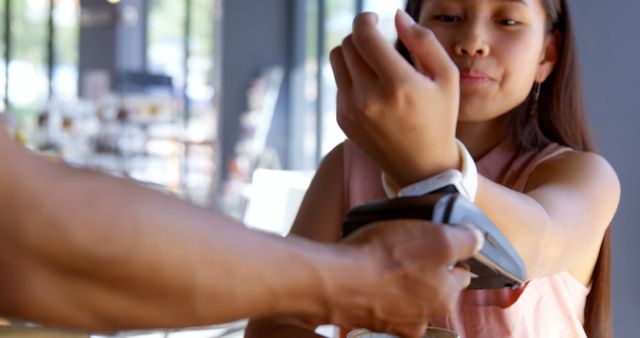 Young woman is using a smartwatch to complete a contactless payment transaction at a cafe. Useful for illustrating technology in daily life, digital wallets, and modern conveniences in retail.