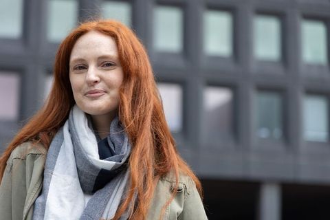 Confident red-haired woman smiling in urban portrait wearing striped scarf and khaki jacket