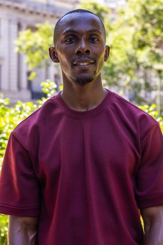 Confident african american man in maroon shirt standing in urban plaza with architecture