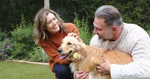 Couple Playing with Golden Retriever in Backyard Garden, Laughing and Sharing Tennis Ball
