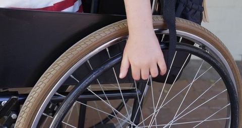 Teenage boy resting hand on wheelchair push rim with red-striped top and strap