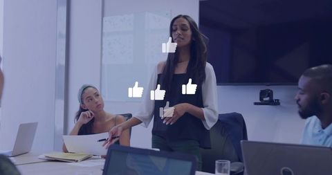 Confident woman presenting to diverse team in modern boardroom with digital engagement icons