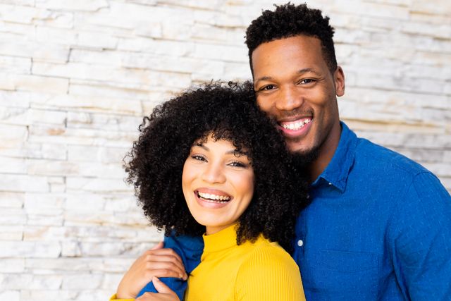 Image of a happy biracial couple embracing and smiling at home. Perfect for illustrating themes of inclusivity, relationships, togetherness, domestic life, and leisure time. Suitable for use in advertisements, blogs, relationship counseling promotions, and social media content.